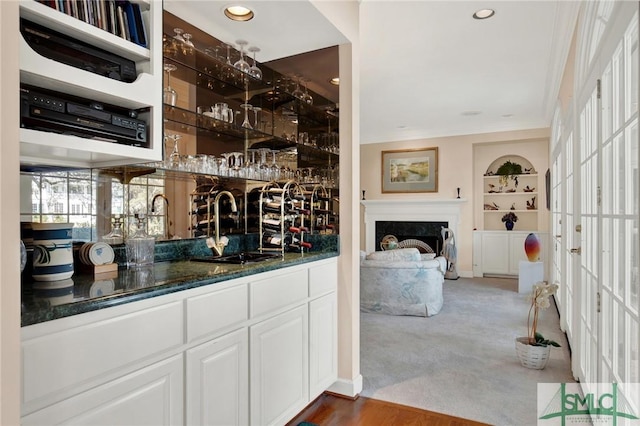 bar with sink, white cabinetry, dark stone counters, built in features, and a high end fireplace