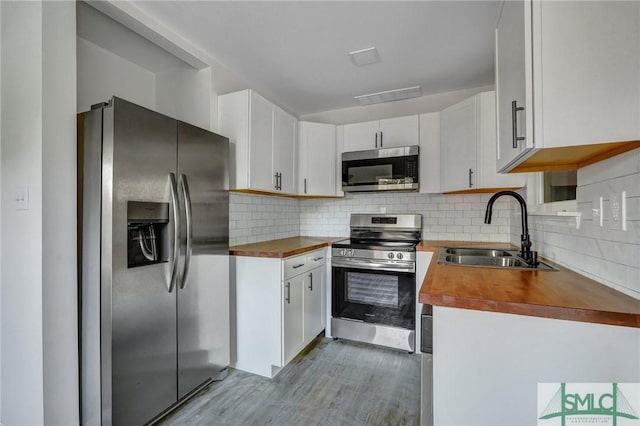 kitchen with stainless steel appliances, wooden counters, sink, and white cabinets