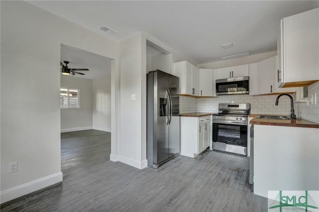 kitchen with butcher block countertops, sink, appliances with stainless steel finishes, white cabinets, and decorative backsplash