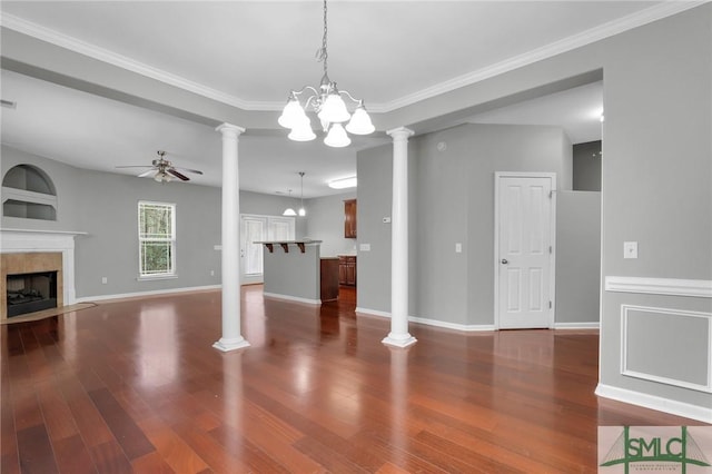 unfurnished living room featuring decorative columns, ornamental molding, hardwood / wood-style floors, a tiled fireplace, and ceiling fan with notable chandelier