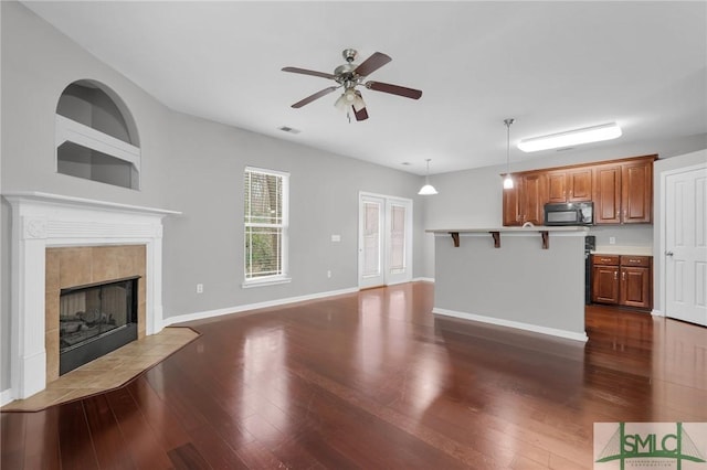 unfurnished living room featuring a tile fireplace, ceiling fan, dark hardwood / wood-style flooring, and built in shelves