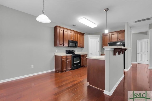 kitchen with decorative light fixtures, dark wood-type flooring, black appliances, and a kitchen breakfast bar