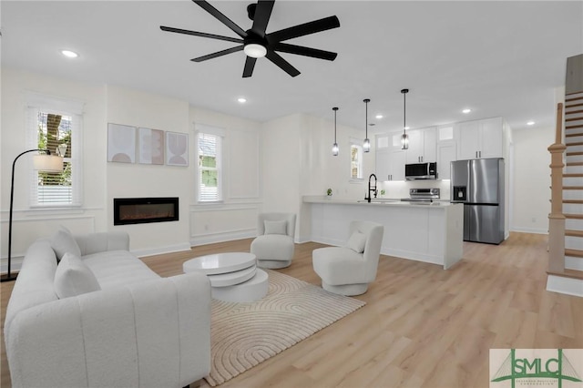 living room with a healthy amount of sunlight, sink, ceiling fan, and light hardwood / wood-style floors