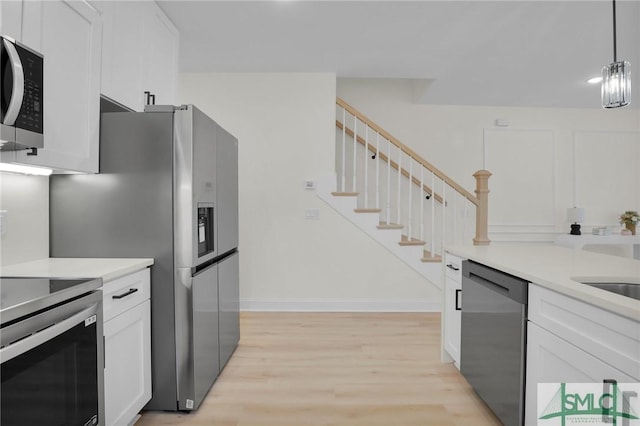 kitchen featuring decorative light fixtures, white cabinetry, sink, stainless steel appliances, and light wood-type flooring