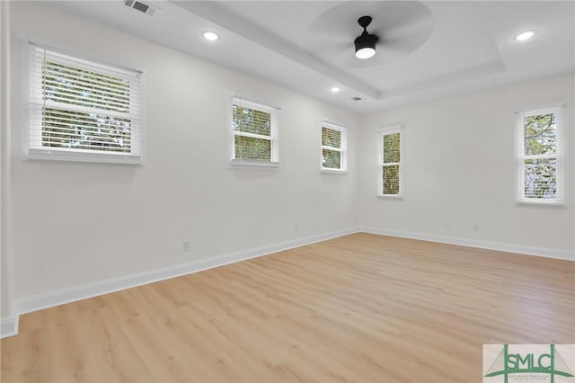 empty room with ceiling fan, a raised ceiling, and light wood-type flooring