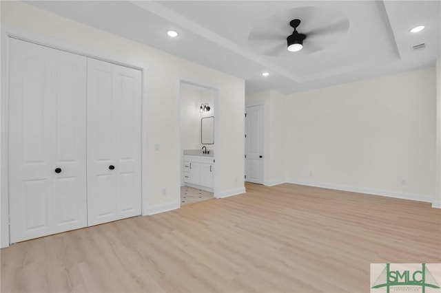 unfurnished bedroom featuring connected bathroom, sink, light hardwood / wood-style floors, a raised ceiling, and a closet