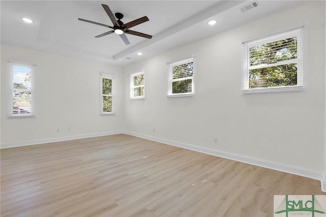 unfurnished room featuring ceiling fan, a tray ceiling, light hardwood / wood-style floors, and a healthy amount of sunlight