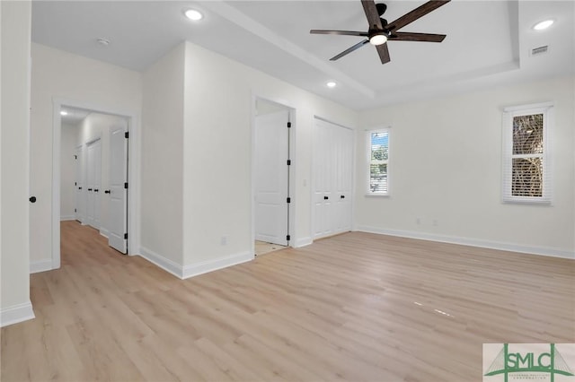 spare room with a tray ceiling, light hardwood / wood-style floors, and ceiling fan