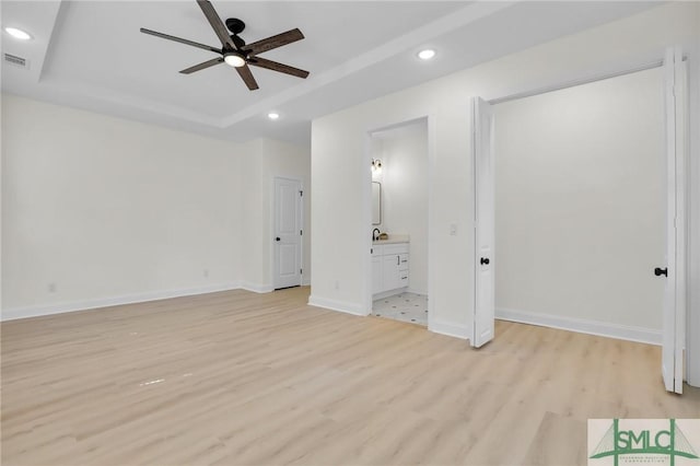 unfurnished bedroom with ensuite bath, light hardwood / wood-style floors, and a raised ceiling