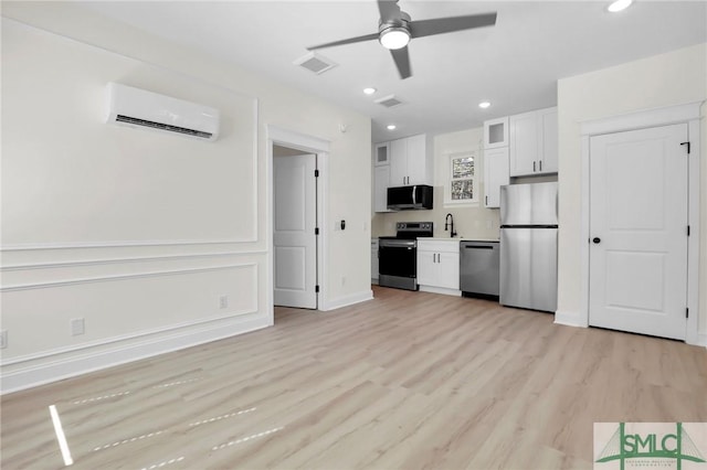 kitchen with a wall mounted air conditioner, white cabinetry, ceiling fan, stainless steel appliances, and light wood-type flooring