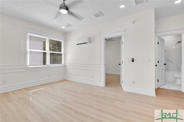 unfurnished bedroom featuring a wall mounted air conditioner, ensuite bath, light hardwood / wood-style flooring, and ceiling fan