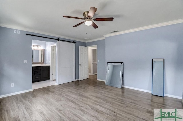 unfurnished bedroom with ensuite bath, ornamental molding, a barn door, and light hardwood / wood-style flooring