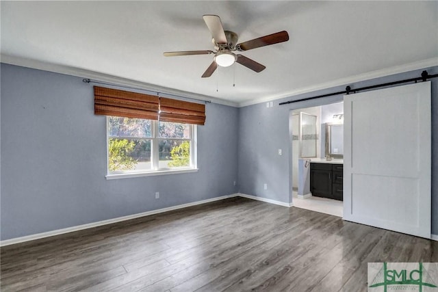 unfurnished living room featuring hardwood / wood-style floors, ornamental molding, a barn door, and ceiling fan