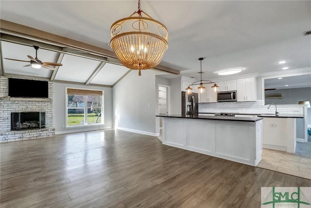 kitchen with pendant lighting, backsplash, stainless steel appliances, white cabinets, and a brick fireplace