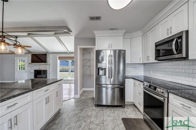 kitchen featuring a brick fireplace, appliances with stainless steel finishes, pendant lighting, ceiling fan, and white cabinets