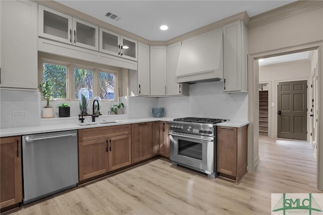 kitchen featuring sink, appliances with stainless steel finishes, light hardwood / wood-style floors, white cabinets, and custom exhaust hood