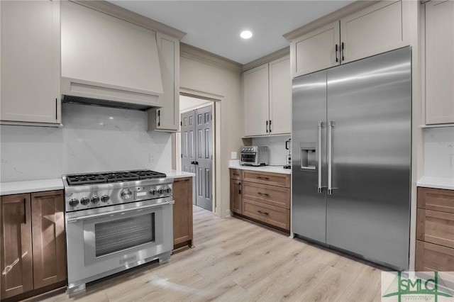 kitchen featuring high quality appliances, premium range hood, and light hardwood / wood-style floors