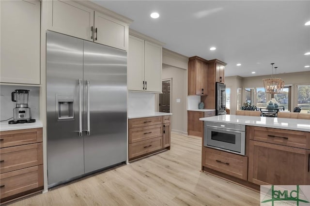 kitchen with built in refrigerator, hanging light fixtures, a notable chandelier, cream cabinets, and light wood-type flooring