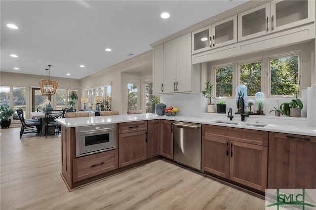 kitchen with sink, decorative light fixtures, stainless steel dishwasher, and light wood-type flooring