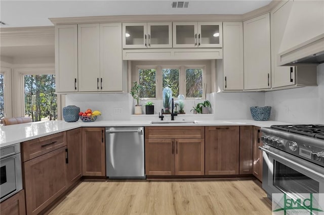 kitchen featuring premium range hood, sink, light wood-type flooring, appliances with stainless steel finishes, and cream cabinets