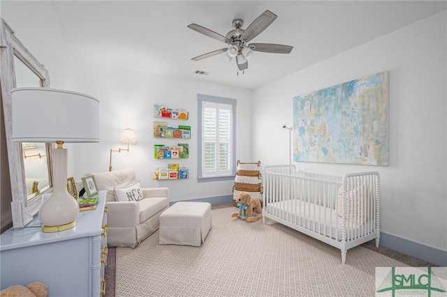 bedroom with a crib, light colored carpet, and ceiling fan