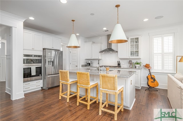 kitchen with wall chimney range hood, a kitchen bar, white cabinets, and appliances with stainless steel finishes