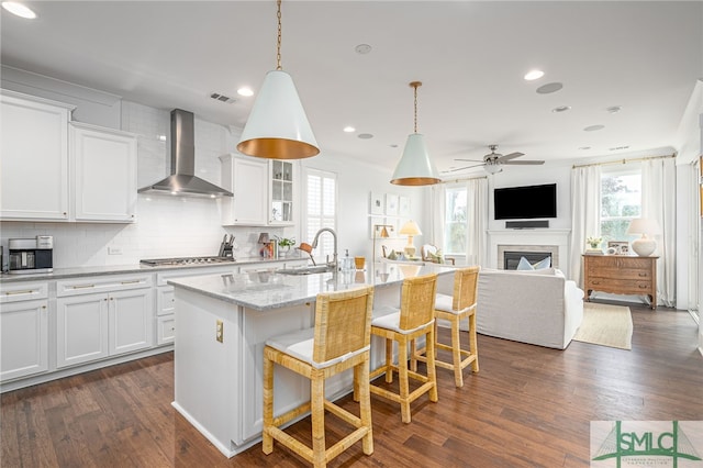 kitchen with sink, white cabinets, wall chimney exhaust hood, and a center island with sink