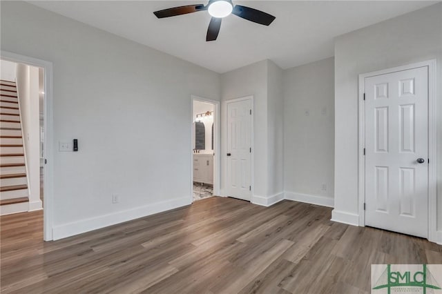 unfurnished bedroom with ensuite bath, a walk in closet, a closet, ceiling fan, and hardwood / wood-style floors