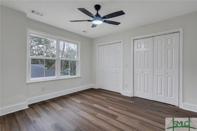 unfurnished bedroom featuring dark hardwood / wood-style flooring, two closets, and ceiling fan