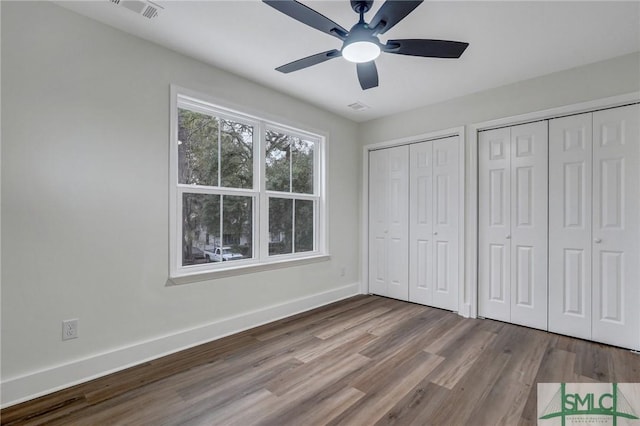 unfurnished bedroom with ceiling fan, light hardwood / wood-style floors, and two closets