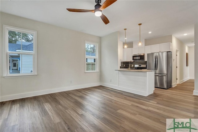 kitchen with wood-type flooring, hanging light fixtures, appliances with stainless steel finishes, kitchen peninsula, and white cabinets