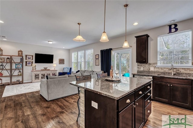 kitchen with light stone counters, a center island, sink, and dark brown cabinets