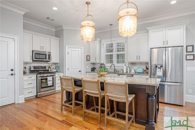 kitchen featuring hanging light fixtures, a center island, white cabinets, and appliances with stainless steel finishes