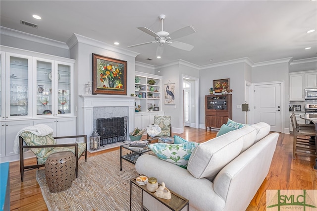 living room featuring a premium fireplace, ornamental molding, ceiling fan, and light hardwood / wood-style floors