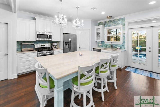 kitchen featuring hanging light fixtures, stainless steel appliances, ornamental molding, white cabinets, and a kitchen island