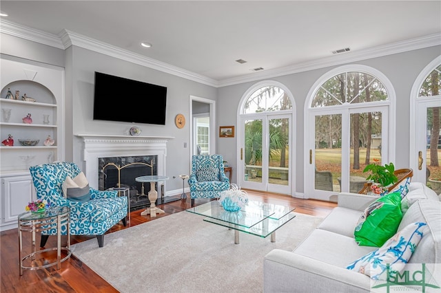 living room with hardwood / wood-style flooring, crown molding, a fireplace, and built in shelves