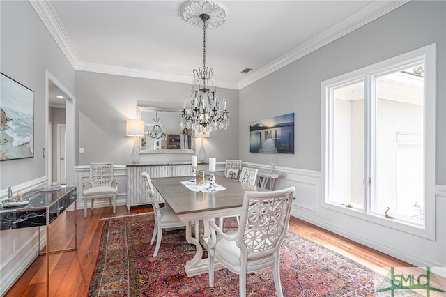 dining room with hardwood / wood-style flooring, crown molding, and an inviting chandelier