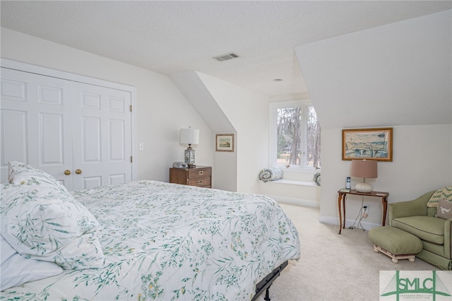 bedroom with light colored carpet, lofted ceiling, a closet, and a textured ceiling