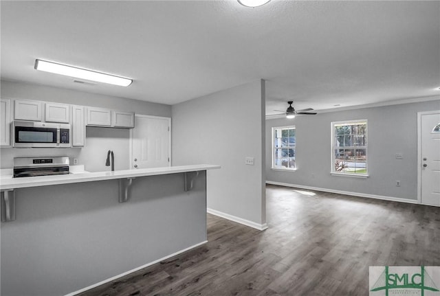 kitchen with sink, white cabinets, a kitchen breakfast bar, stove, and dark wood-type flooring