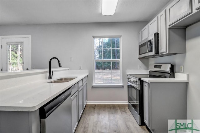 kitchen featuring appliances with stainless steel finishes, sink, light wood-type flooring, and kitchen peninsula