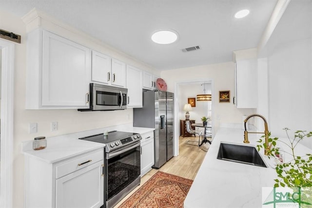 kitchen with light wood-type flooring, appliances with stainless steel finishes, sink, and white cabinets