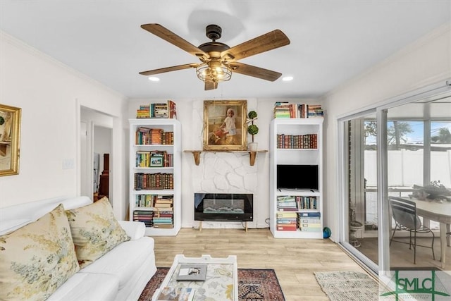 living room featuring ornamental molding, a large fireplace, ceiling fan, and light hardwood / wood-style floors