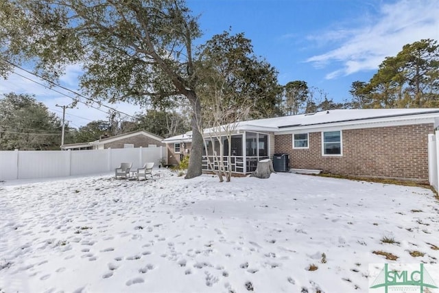 snow covered back of property featuring a sunroom and central air condition unit