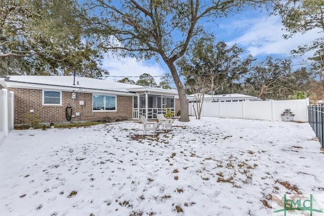 snow covered back of property featuring a sunroom