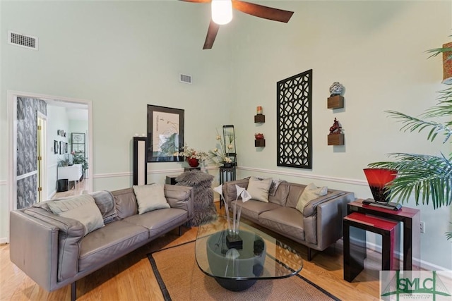 living room with ceiling fan, a high ceiling, and light wood-type flooring