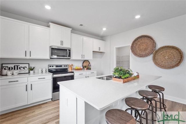 kitchen featuring a breakfast bar area, a center island with sink, stainless steel appliances, light hardwood / wood-style floors, and white cabinets