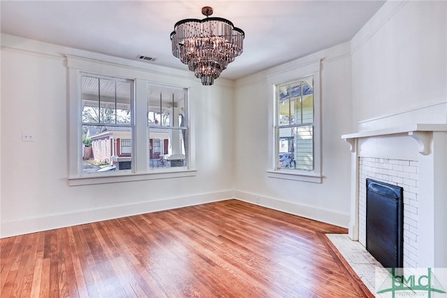 unfurnished dining area featuring a notable chandelier, hardwood / wood-style flooring, and a fireplace