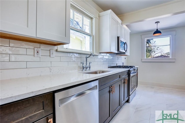 kitchen with pendant lighting, sink, appliances with stainless steel finishes, light stone countertops, and white cabinets