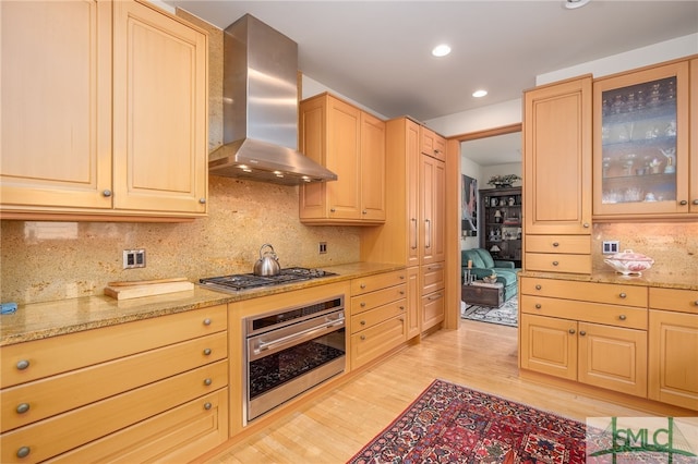 kitchen featuring light stone counters, light brown cabinetry, wall chimney exhaust hood, and appliances with stainless steel finishes