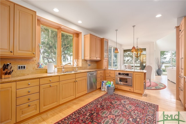 kitchen with pendant lighting, sink, appliances with stainless steel finishes, light hardwood / wood-style floors, and light stone countertops